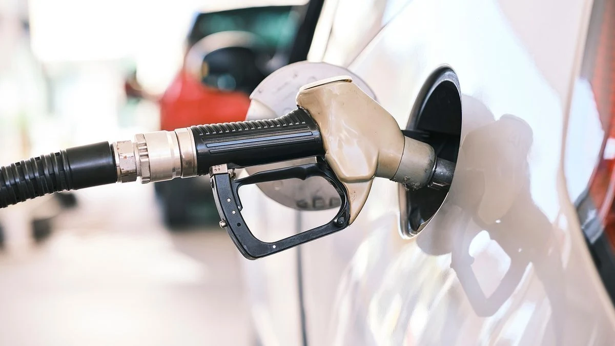 Primer plano de la boquilla de una gasolinera insertada en el depósito de un coche, al atardecer, sin personas visibles