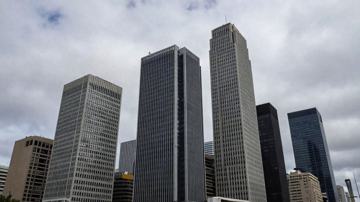 Illustrative image: view of an urban landscape with modern financial buildings under a cloudy sky, representing AI's impact on the economy.