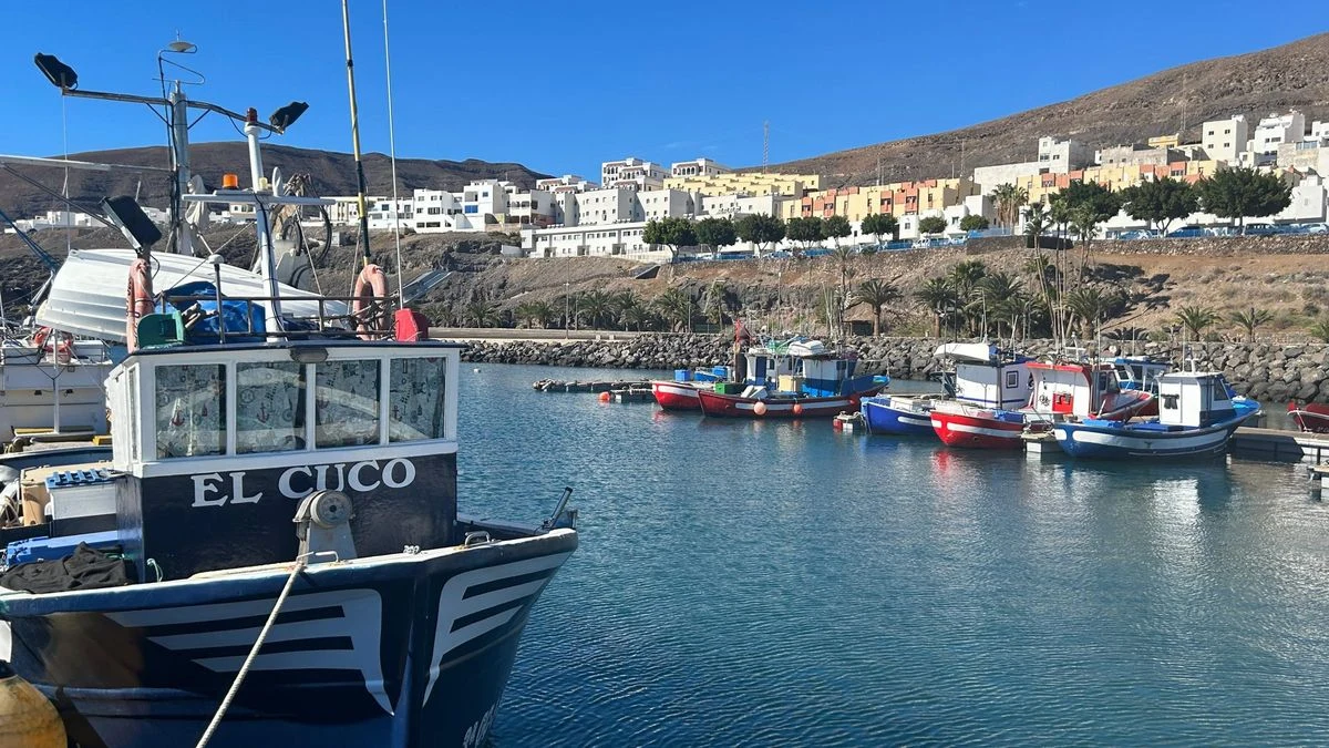 Imagen ilustrativa: un barco pesquero atracado en un puerto al atardecer, con el cielo anaranjado y reflejos en el agua.
