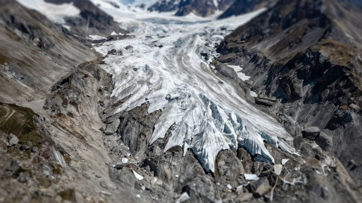 Illustrative image: aerial view of a mountainous area affected by climate change, showing melting glaciers and unstable terrain.