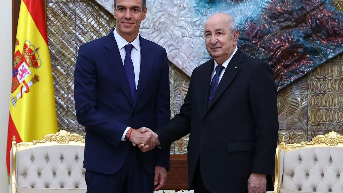 Primer plano de una válvula de gasoducto con banderas de España y Argelia desenfocadas al fondo