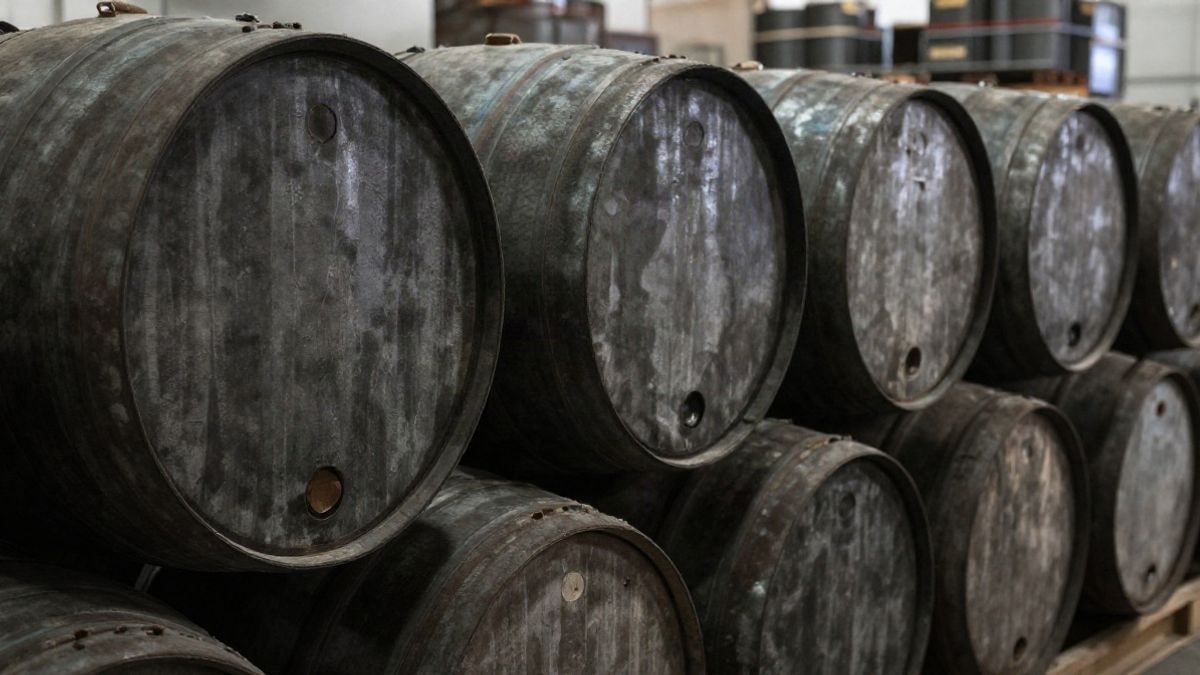 Illustrative image: stacked oil barrels in a warehouse, showing metal details, with dramatic natural light.