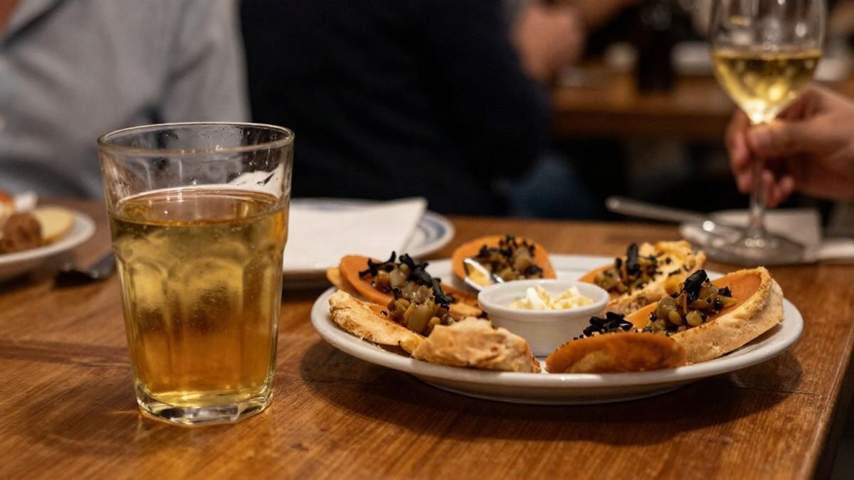 Illustrative image: glass of cider and snacks on a wooden table at a night event with blurred background lights.