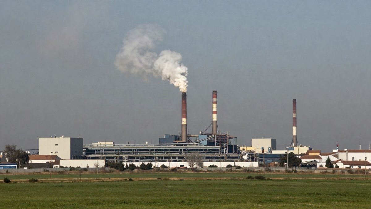 Imagen ilustrativa: una fábrica de textiles en la distancia, con humo industrial y contaminación al fondo, contrastando con un paisaje verde en primer plano.